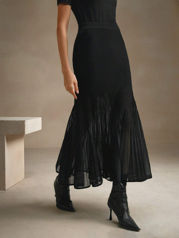 Person wearing a black pleated dress with high-heeled boots in a minimalistic setting