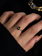 Gold ring with a black stone on a person's finger against a dark background