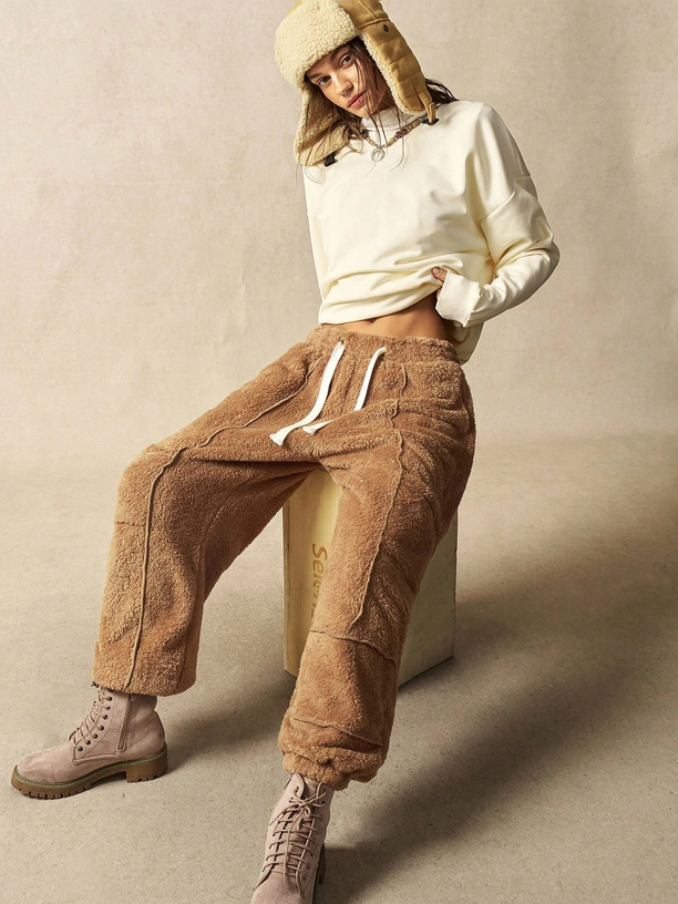 Person wearing a cream sweater, brown pants, and beige hat sitting on a beige block.
