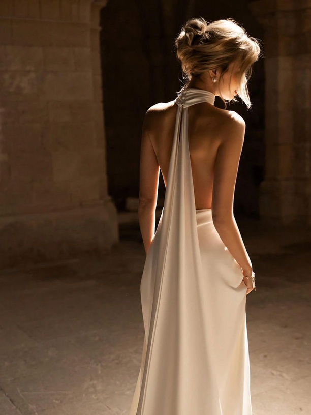 Woman in a white dress with a flowing fabric detail, standing in a dimly lit room.