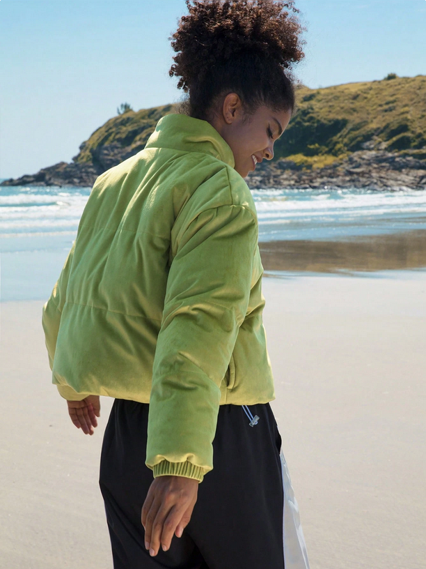 Person wearing a bright green jacket on a beach with ocean and hills in the background