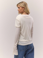 Woman wearing a light gray long-sleeve top and blue jeans on a plain background