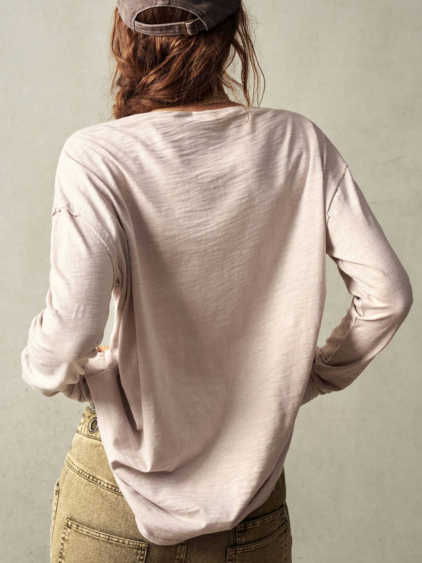 Person wearing a light pink long-sleeve shirt and beige pants against a plain background