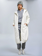 Person wearing a long white quilted coat over a gray outfit on a plain background