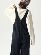 Person wearing black overalls and a cream sweatshirt on a light gray background