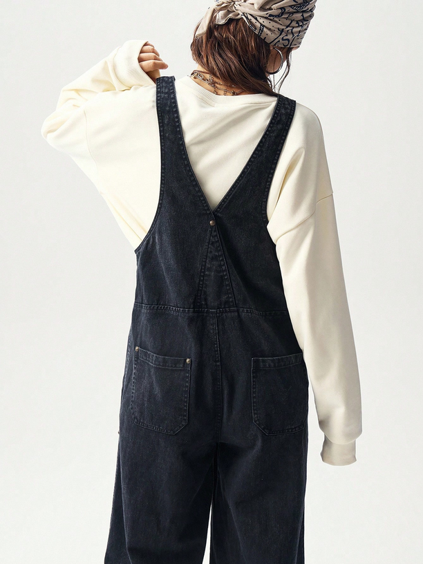 Person wearing black overalls and a cream sweatshirt on a light gray background