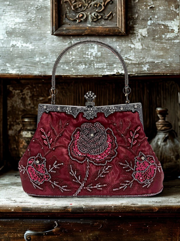 Vintage burgundy handbag with floral embroidery on a wooden surface.