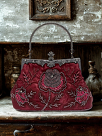 Vintage burgundy handbag with floral embroidery on a wooden surface.
