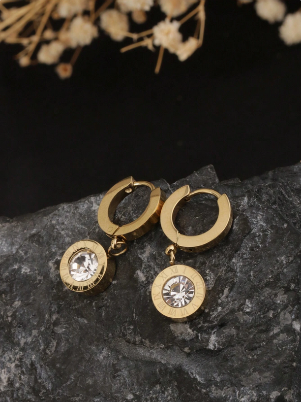 Gold hoop earrings with crystal drops on a dark stone surface