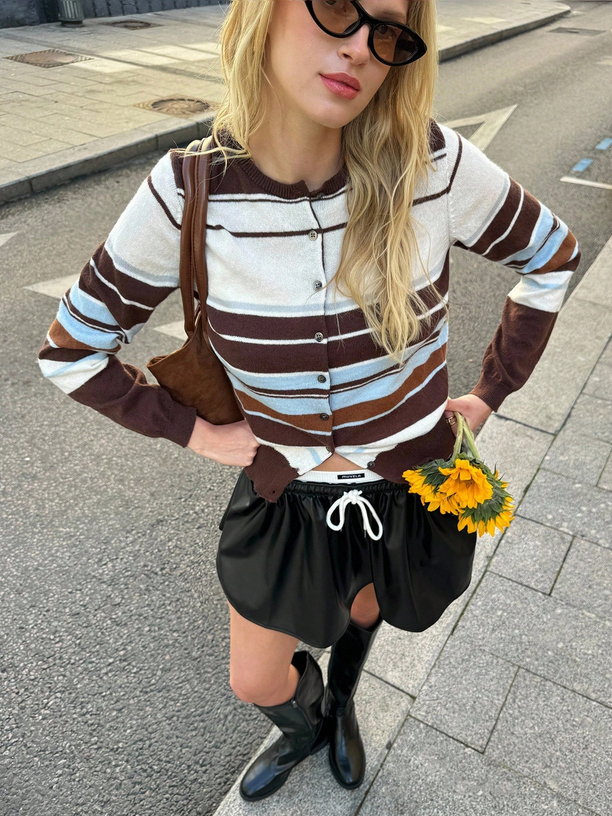 Person wearing a striped sweater and black skirt holding flowers on a street.