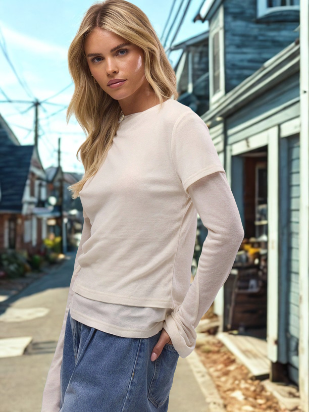 Woman wearing a light-colored long-sleeve shirt and blue jeans standing on a street.