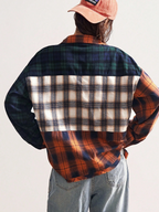 Person wearing a plaid shirt with a patchwork pattern on a plain background
