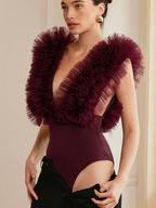 Woman wearing a burgundy bodysuit with ruffled shoulder details against a neutral background