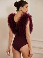 Woman wearing a burgundy swimsuit with ruffled shoulder details against a neutral background